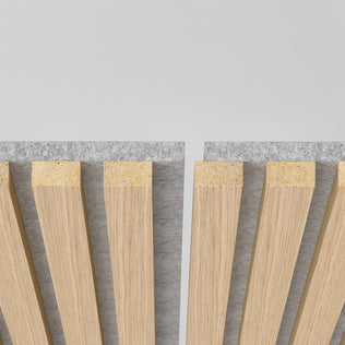 A close-up of two sections of Artika Sonolok 15.5 ft sound-absorbing wall panel kit, featuring vertical wooden slats on gray felt backing with a narrow gap, set against a light background.