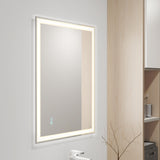 A rectangular wall-mounted mirror with built-in LED lighting around the edges is shown in a modern bathroom with light wood accents and minimalistic decor.