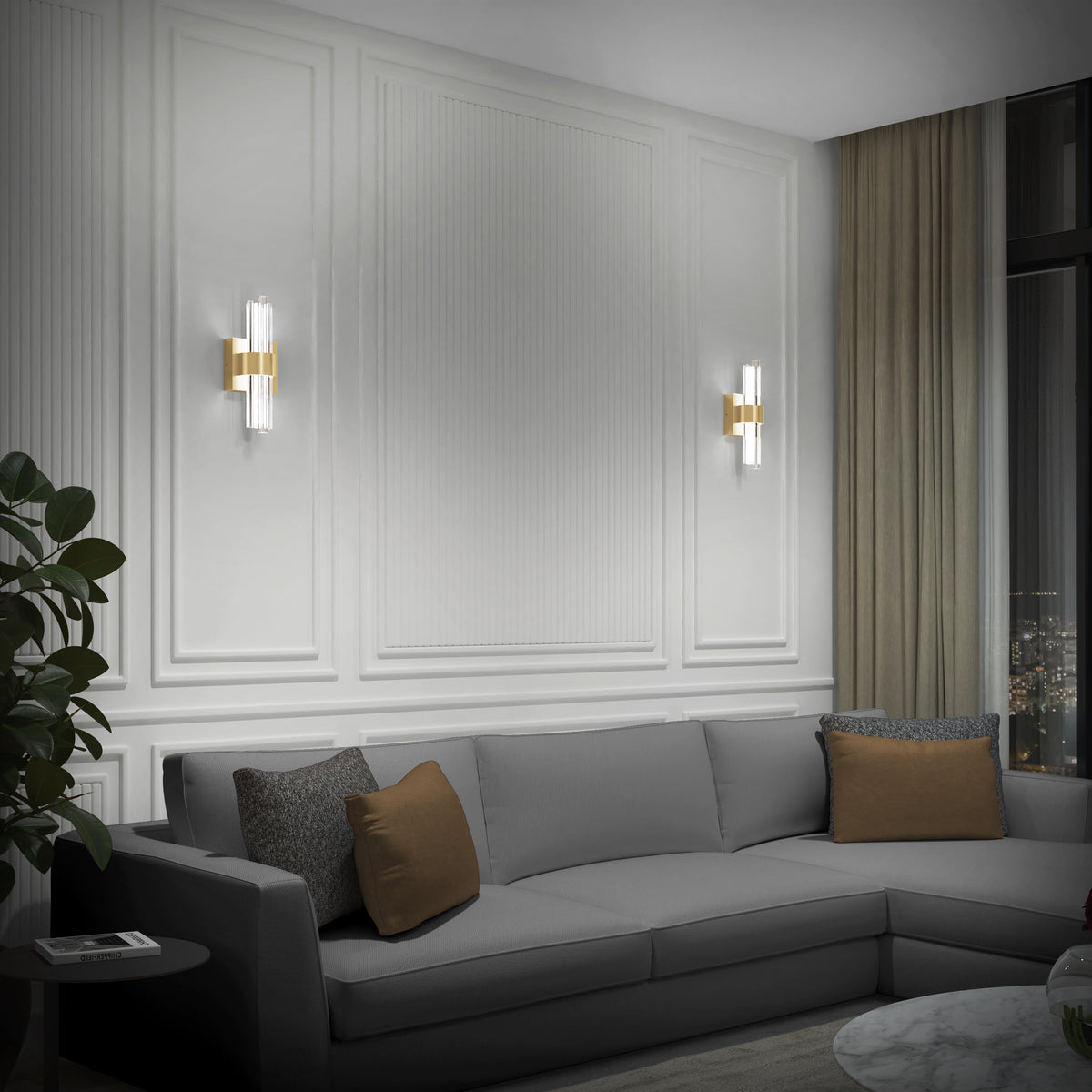 A modern living room with a gray sectional sofa, brown and gray cushions, wall-mounted sconces, white paneled walls, a marble coffee table, a plant, and large windows with beige curtains showing a city view at night.