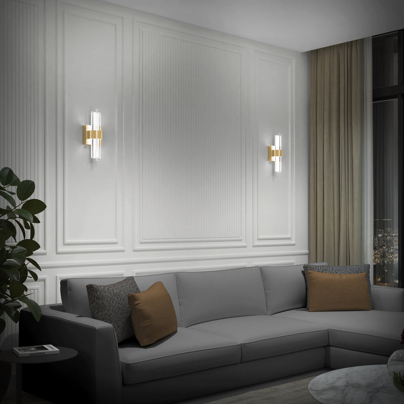 A modern living room features a gray sectional, brown and gray pillows, white paneled walls, a potted plant, beige curtains framing a night city view, and Artika's Dorado contemporary LED wall sconce 3 CCT for luxurious lighting.