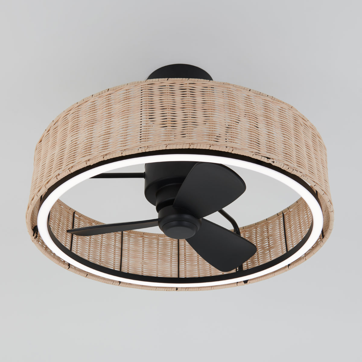 A ceiling fan with black blades and a built-in LED light ring, enclosed by a round, woven rattan shade, mounted on a white ceiling.