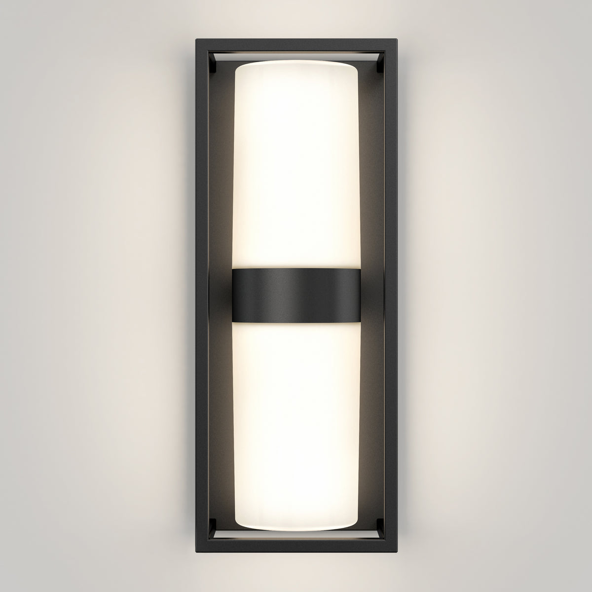 A modern wall sconce with a rectangular black frame and a central horizontal black band, featuring a frosted white cylindrical light emitting a soft glow against a light-colored wall.