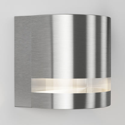 The Artika Valor Round LED indoor-outdoor wall light features a modern, curved design with a brushed metal finish and a horizontal frosted slit that emits soft white light.
