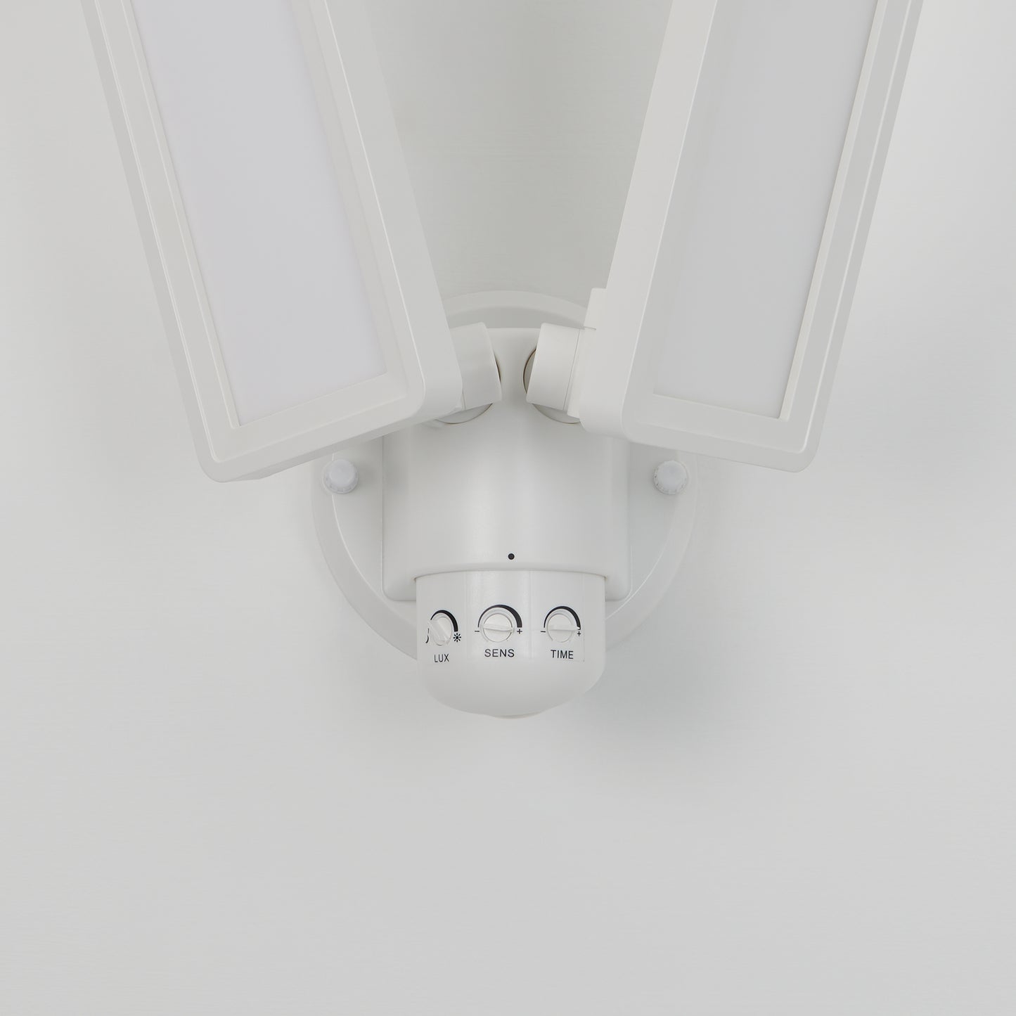 A close-up of the Artika Sentinel outdoor Flat Panel Security light, a white dual-head LED fixture with “LUX,” “SENS,” and “TIME” control dials on its base, mounted on a white wall.