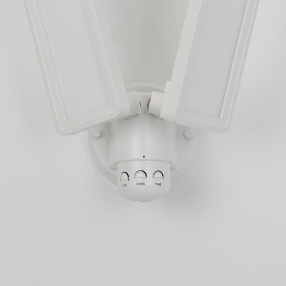 A close-up of the Artika Sentinel outdoor Flat Panel Security light, a white dual-head LED fixture with “LUX,” “SENS,” and “TIME” control dials on its base, mounted on a white wall.