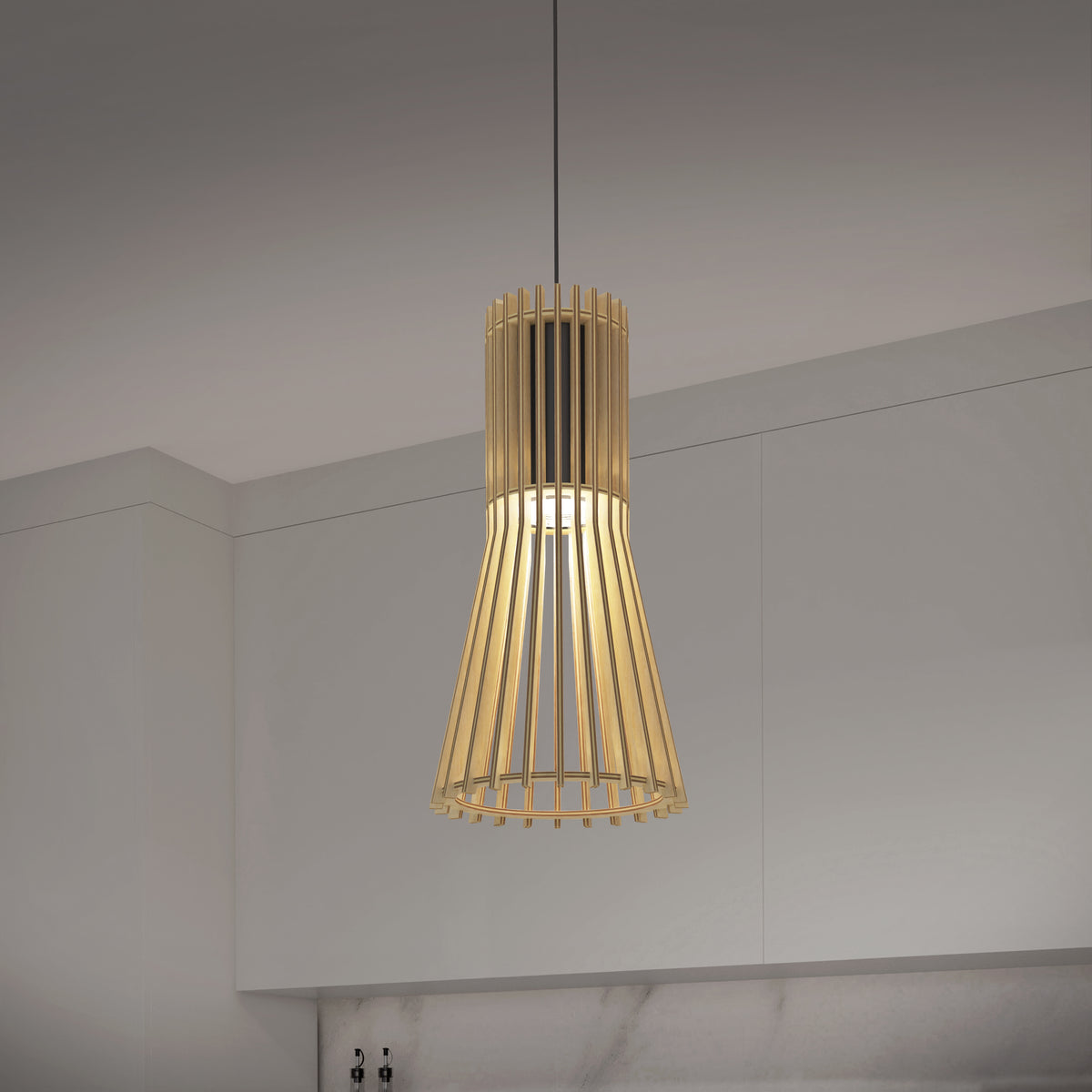 A modern pendant light with a wooden slatted design hangs from the ceiling in a minimalist kitchen with white cabinets and a marble backsplash.