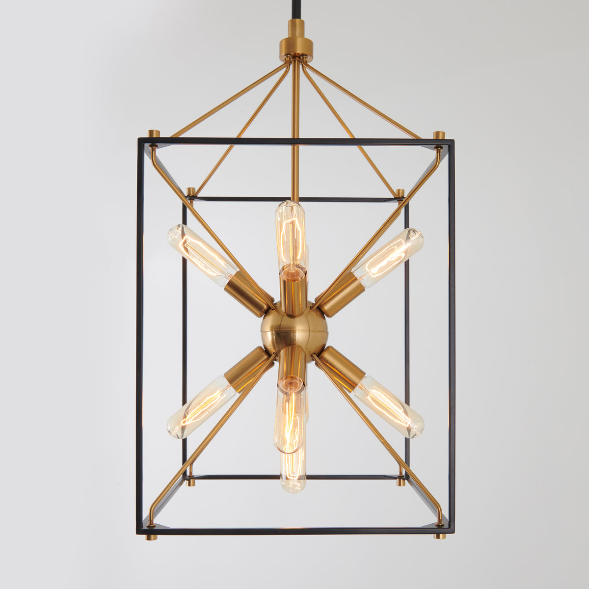 A modern pendant light with a geometric, open-frame rectangular design in black and brass, featuring a central brass sphere with six exposed Edison bulbs radiating outward in a star-like pattern.