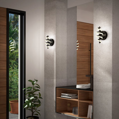 A modern interior with a wall mirror, wooden shelving, two Artika Chorus LED Wall Lights in black and gold, a potted plant, and an open door revealing greenery outside.