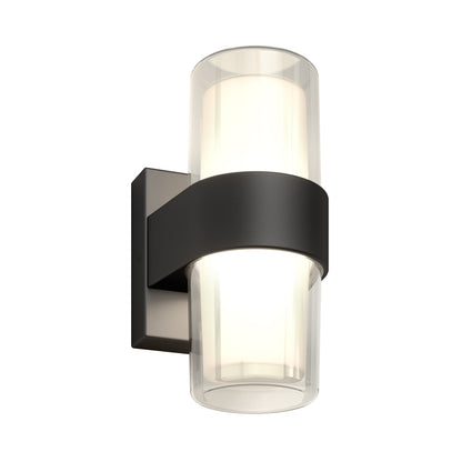The Artika Colton modern LED indoor-outdoor wall light 5 CCT features a cylindrical frosted glass shade inside clear glass, highlighted by a dark metal band and mounted on a black rectangular base for contemporary style.