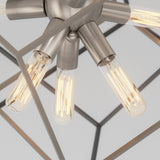 Close-up of a modern ceiling light fixture with exposed filament bulbs and a geometric metal frame, viewed from below. The fixture has a brushed metal finish and emits a warm glow.