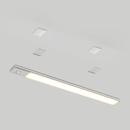 The Artika Outline under cabinet LED light 3CCT, a slim rectangular fixture with a metallic finish, is mounted on a white ceiling with four small square ceiling features symmetrically placed above it.
