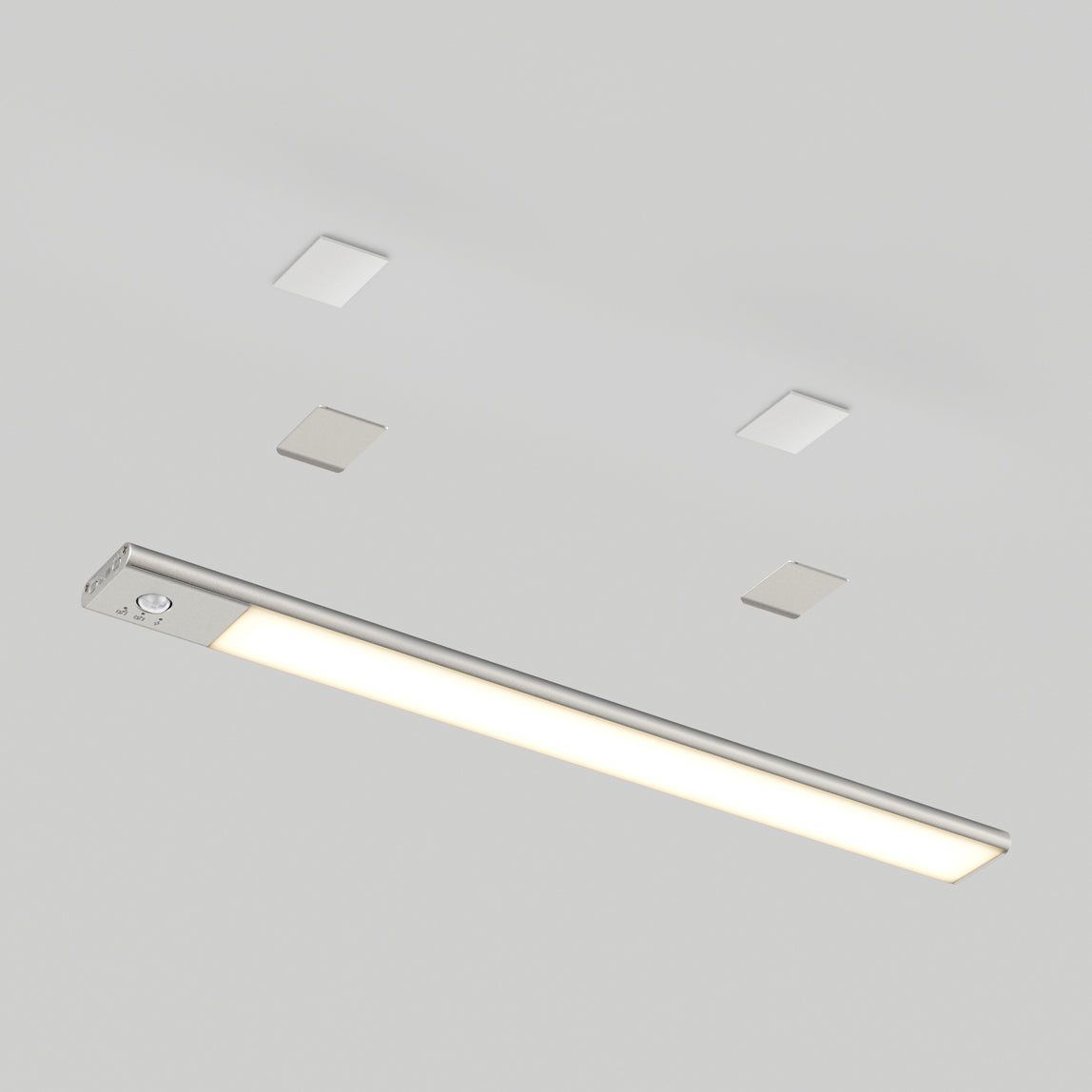 A slim, rectangular LED ceiling light fixture with a metallic finish is installed on a white ceiling, accompanied by four small square-shaped ceiling elements in two rows above it.