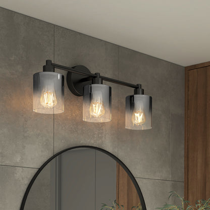 The Artika Haze modern 3-light bathroom vanity light features black metal and glass shades, each with a bulb, mounted above a round mirror on gray tile, with a wooden panel and greenery partially visible.