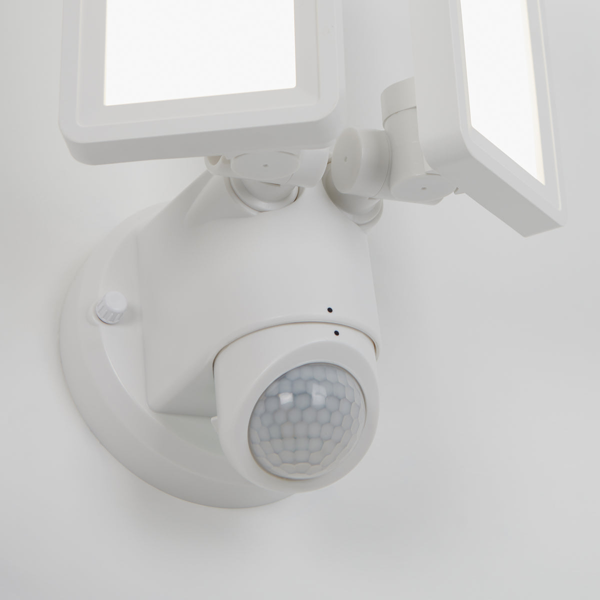 A close-up view of a white outdoor motion sensor light with two rectangular LED panels and a round motion detector on a wall.
