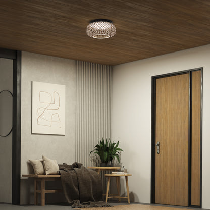 A modern entryway features a wooden ceiling, Artikas Benson 15 in. LED flush mount light, a wooden door, bench with blankets, potted plant on a table, and minimalist abstract wall art.