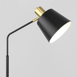 A modern black floor lamp with a gold accent near the top, featuring a conical shade angled downward, set against a plain light gray background.