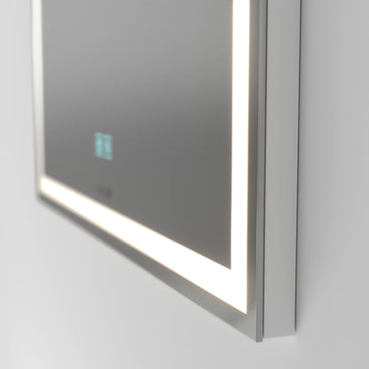A close-up of the Artika Aurea anti fog LED wall mirror shows its modern rectangular design, edge-lit LEDs, and a small digital display on the bottom left corner, all mounted on a light-colored wall.