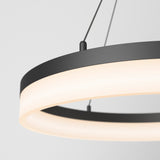 A close-up of a modern, circular pendant light with a black frame and a glowing white diffuser, suspended by two thin cables against a plain white background.