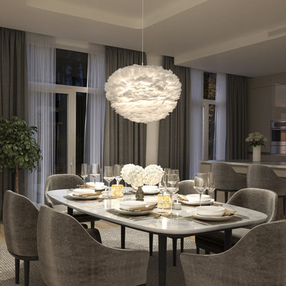 A modern dining room features a marble table for six, gray upholstered chairs, elegant place settings, large windows with sheer curtains, and a Plume LED pendant light by Artika above white flowers at the center of the table.