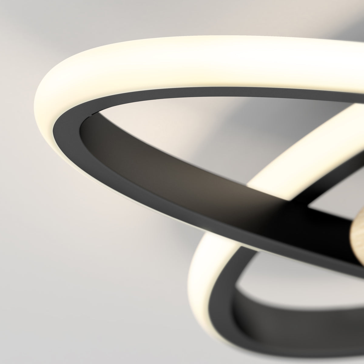 Close-up of a modern ceiling light fixture with curved, overlapping LED strips emitting soft white light against a neutral background. The fixture features sleek black and white elements.