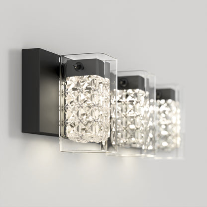 The Artika Crystal Cube LED bathroom vanity light features three rectangular black bases, each with a faceted glass shade, emitting bright sparkling light. This modern wall-mounted fixture adds elegance to any plain light gray wall.