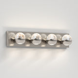 A modern wall-mounted vanity light fixture with four round, clear glass bulb covers, each containing small bubbles, set on a rectangular metallic base against a white wall.