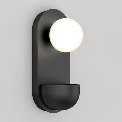 The Artika Bloomfield LED modern mid-century wall sconce 5 CCT features a black finish, a round frosted white globe on top, and a curved bowl-like base, shown mounted on a light gray wall.