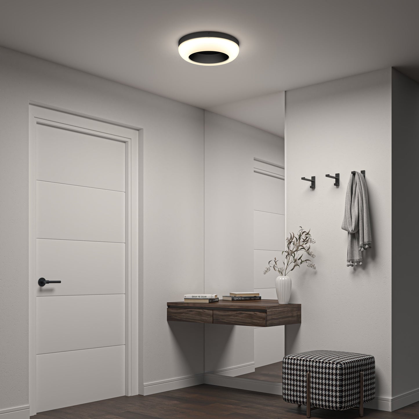 A modern, minimalist entryway features a white door, floating wooden shelf with books and a vase, wall hooks, large mirror, checkered ottoman, and is elegantly lit by the Louka 15 in. modern LED flush mount light 5 CCT from Artika-CAN-dev.