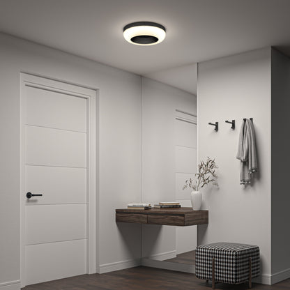 A modern, minimalist entryway features a white door, floating wooden shelf with books and a vase, wall hooks, large mirror, checkered ottoman, and is elegantly lit by the Louka 15 in. modern LED flush mount light 5 CCT from Artika-CAN-dev.