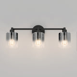 A modern wall sconce light fixture with three exposed bulbs, each enclosed in a clear cylindrical glass shade, mounted on a black horizontal bar against a light gray wall.
