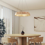 A modern dining area with a round wooden table, four matching chairs, a black vase with branches, a large abstract artwork on the wall, a potted plant, and a wooden pendant light hanging from the ceiling.