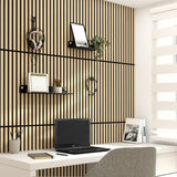 A modern home office with a white desk, laptop, potted plants, shelves, and calendar. The wall features vertical wood slats, and a window with white blinds lets in natural light. A gray chair sits at the desk.