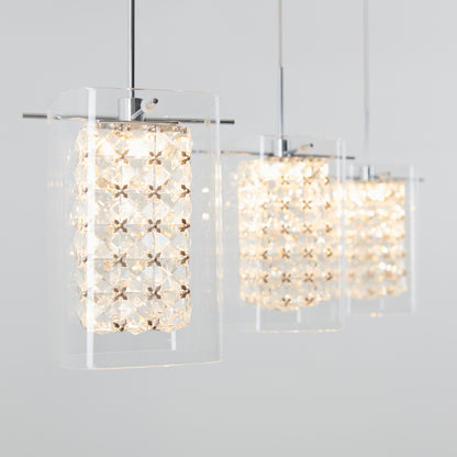 The Artika Crystal Cube 3-light LED pendant light features three modern fixtures with clear glass and geometric crystal-like patterns, hanging in a row and casting a warm, bright glow against a light gray background.
