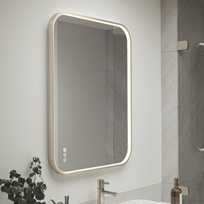The Artika Royce Dimmable LED Mirror, featuring 3 CCT and both horizontal and vertical mount options, hangs above a sink with a gold faucet. A plant and soap dispenser sit on the countertop below the mirror.