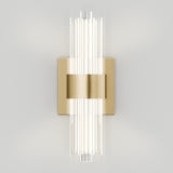 A modern wall sconce with vertical clear glass rods, mounted on a rectangular brass plate, emits bright light against a plain white wall.