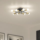 A modern ceiling light fixture with six exposed bulbs arranged on black and gold intersecting rods, illuminating a minimal room with framed artwork on white walls.