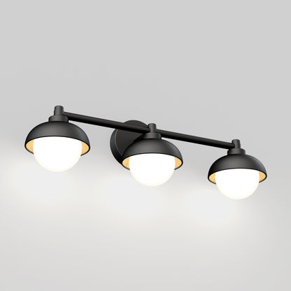 The Artika Boden LED mid-century bathroom vanity light features three round black metal lamp heads with glowing white bulbs, arranged in a row and mounted on a wall.