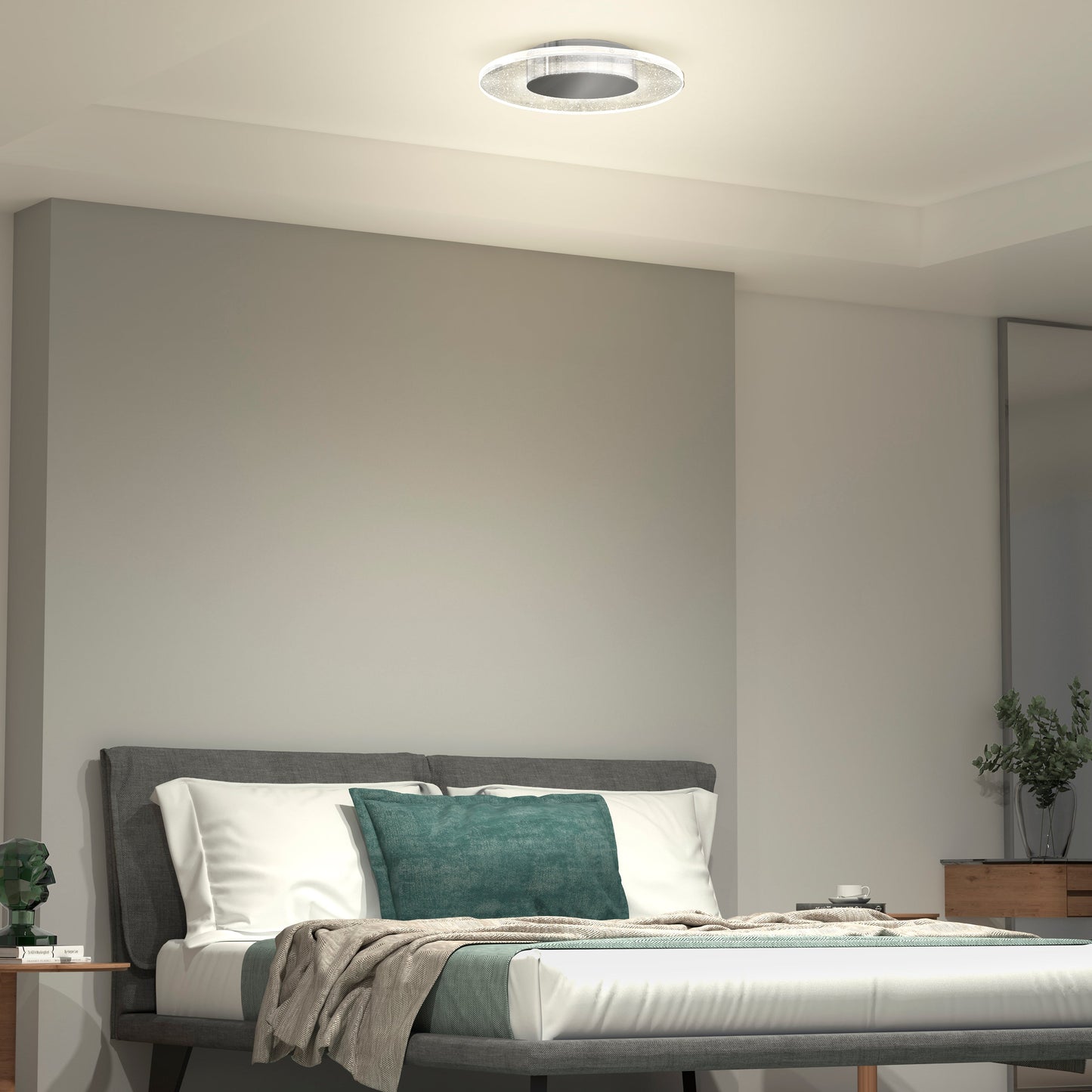A modern bedroom features a gray bed frame, white bedding, teal and beige pillows, a beige throw, wooden nightstand and dresser, potted plants, and the Essence Disk LED flush mount by Artika-CAN-dev with a sleek chrome finish on the white ceiling.