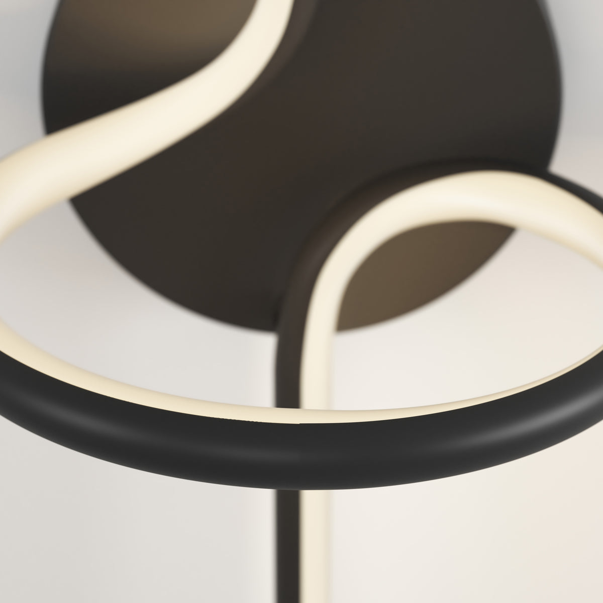A close-up of a modern light fixture with smooth, curved black and white LED tubes against a neutral background. The design features loops and seamless lines.