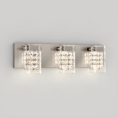 The Artika Crystal Cube LED bathroom vanity light 5 CCT features three rectangular glass sconces with crystal accents, mounted on a brushed metal backplate against a plain light gray wall.