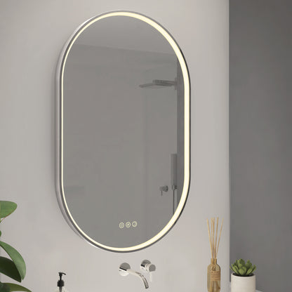 The Artika Royce LED mirror 3 CCT with defogger is mounted above a wall faucet, with small potted plants and a reed diffuser on the counter below. The minimal, modern background enhances its sleek design.