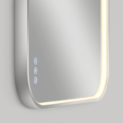 A close-up of a modern rectangular smart mirror with rounded corners and built-in LED lighting along the edge. Three illuminated touch control icons are visible in the lower left corner of the mirror.