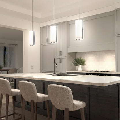 Modern kitchen with a marble island, three upholstered barstools, Artika Subway Round Mini LED pendant lights, light gray cabinets, built-in stove, and a potted plant on the counter. Dining area visible in the background.