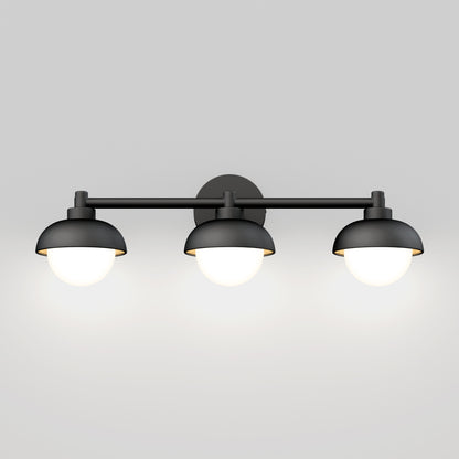 The Artika Boden LED mid-century bathroom vanity light features three black, dome-shaped shades with glowing white bulbs, wall-mounted against a plain light gray background.