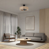 A modern living room with a gray sofa, wooden armchair, round wooden coffee table, large potted plant, and a woven ceiling light fixture. Neutral-toned walls and sheer curtains complete the minimalist decor.