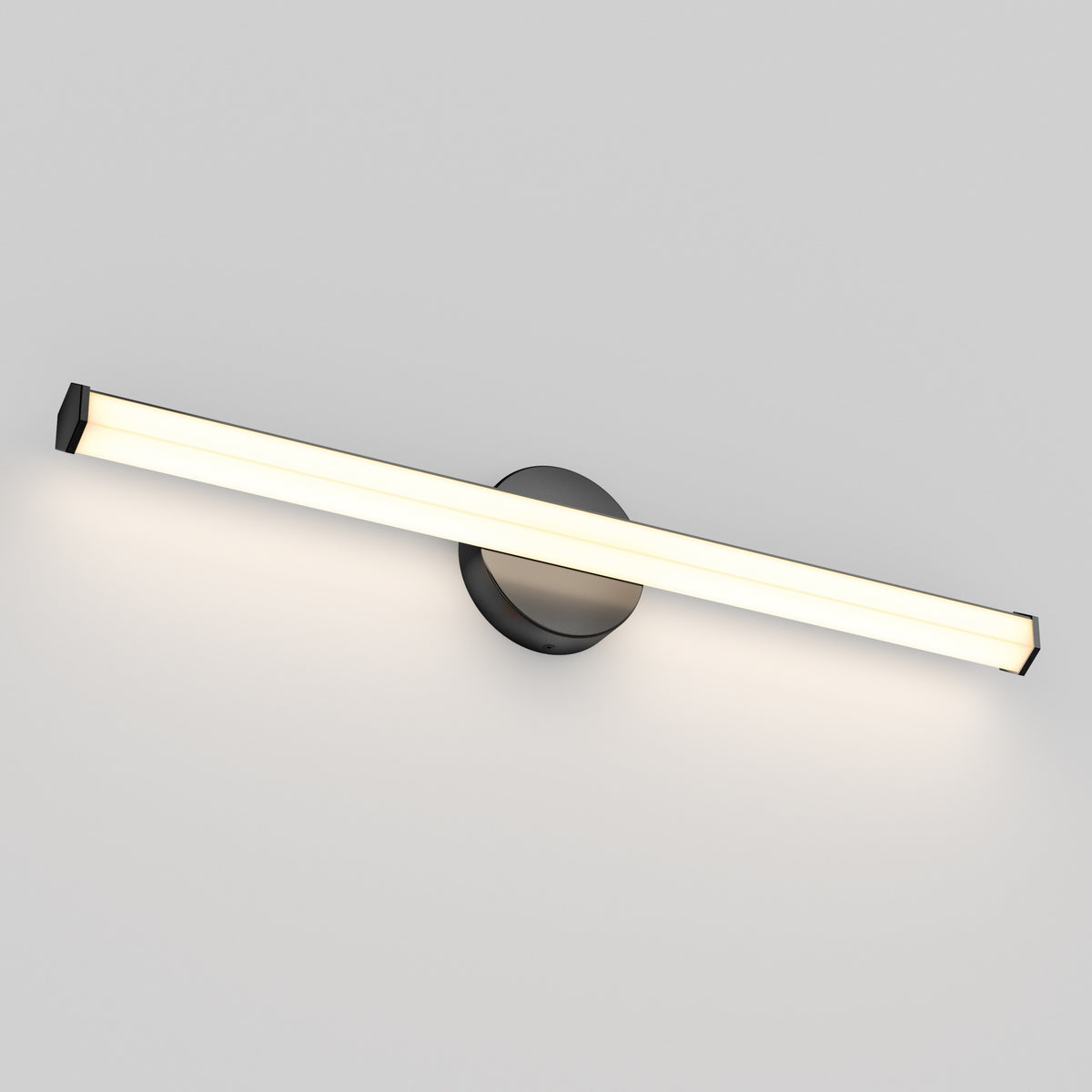 A modern, minimalist wall-mounted LED light fixture with a long, horizontal bar and a round black base, emitting a soft white glow against a plain light gray wall.