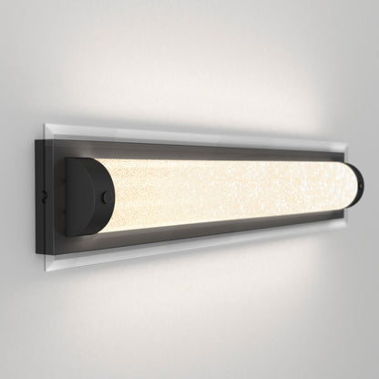 The Artika Glamour LED bathroom vanity light 3 CCT is a modern, rectangular wall sconce featuring a frosted illuminated glass tube and dark metal frame, shown mounted on a light gray wall.