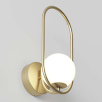 The Artika Bloom LED Sconce 3 CCT features a matte gold oval metal frame and round white frosted glass shade, emitting soft light when mounted on a light grey wall.
