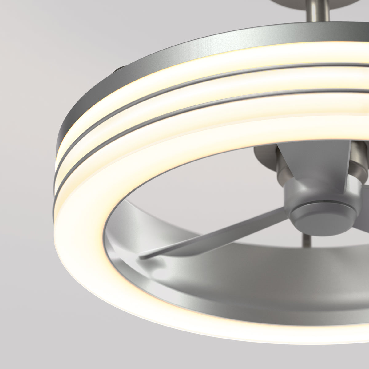 Close-up of a modern ceiling fan with three blades and a circular LED light ring, featuring a sleek, metallic design against a plain, light gray background.