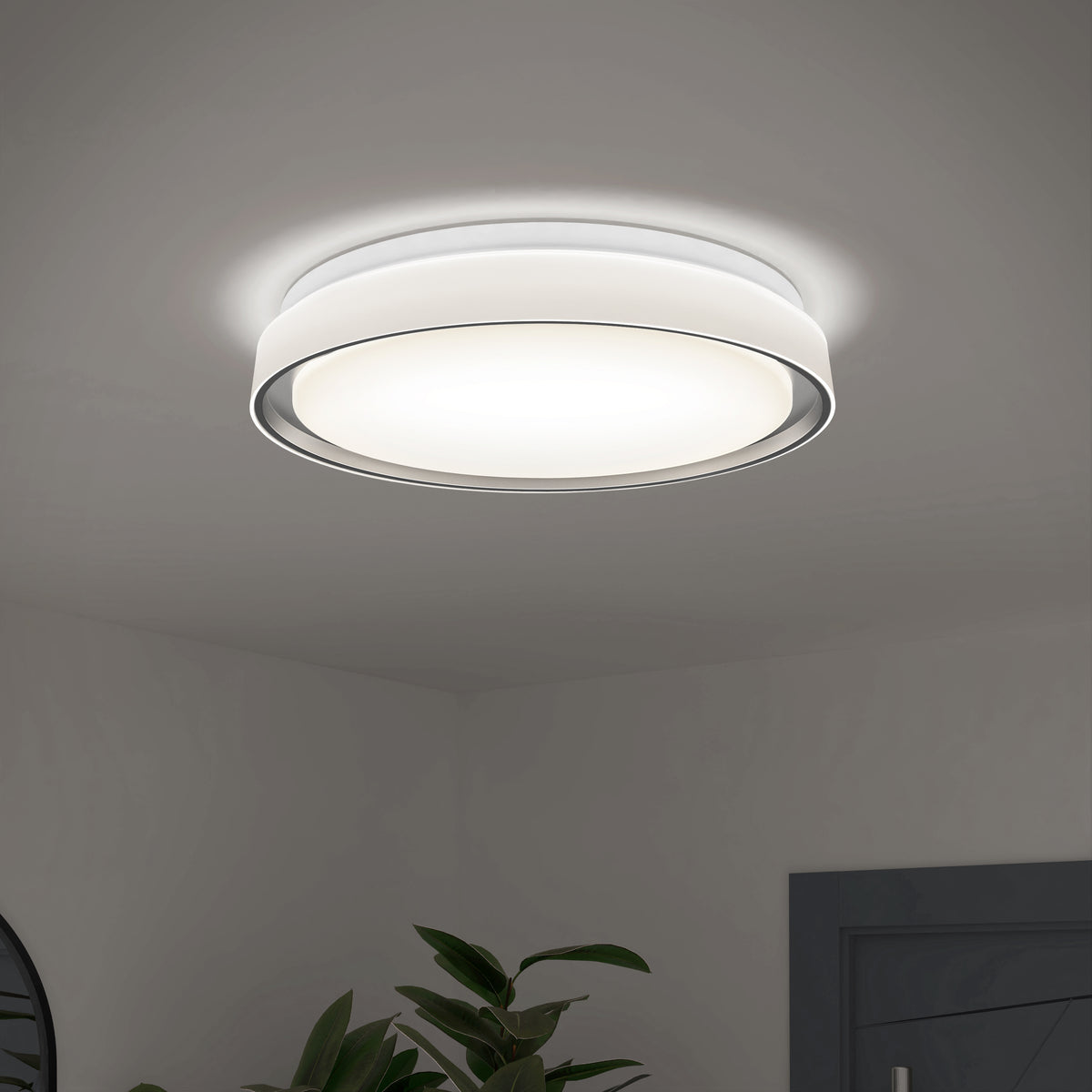 A modern, round ceiling light fixture emits a soft, bright glow in a minimalist room with white walls and a glimpse of green plant leaves below.